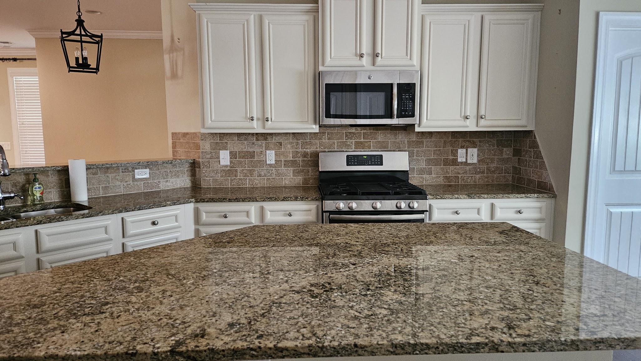 A kitchen with granite island and white cabinets, cleaned by Miranda Cleaning